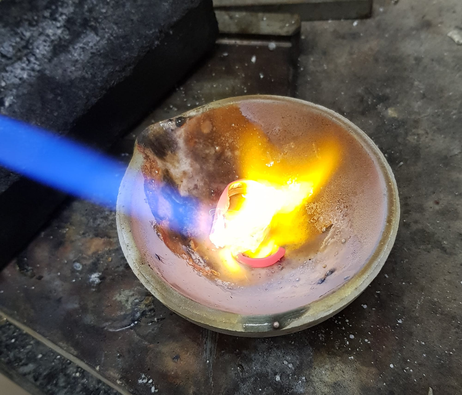 A gold ring glowing white-hot in a crucible under a blue torch flame
