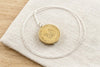 South African brass coin locket necklace resting on linen - Minted Jewellery