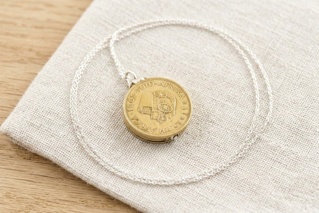 South African brass coin locket necklace resting on linen - Minted Jewellery