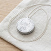 Silver coin diffuser locket resting on linen - Minted Jewellery