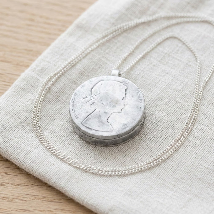 Silver coin diffuser locket resting on linen - Minted Jewellery