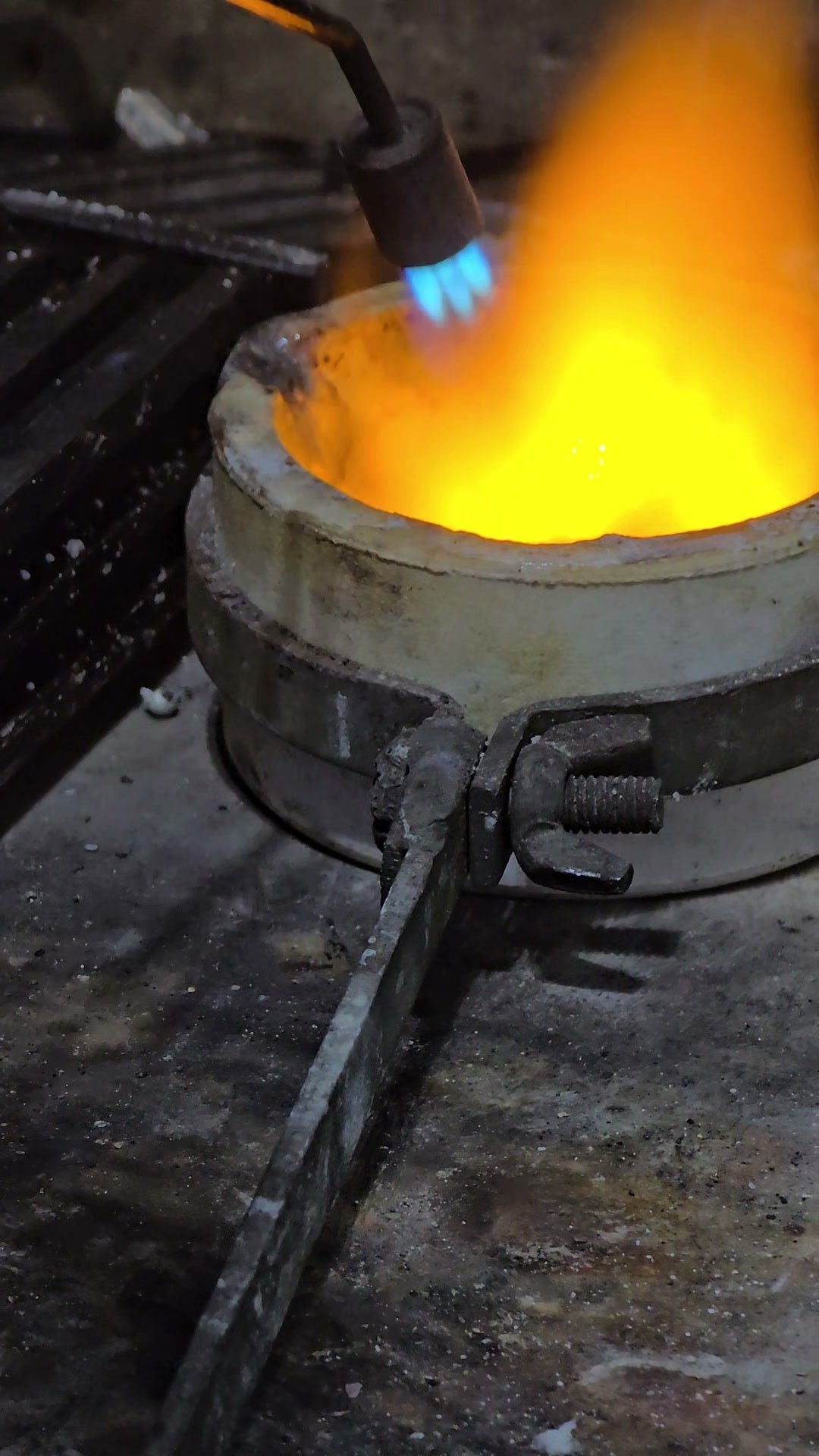 A torch over a crucible of molten gold, a tall orange flame rising from it