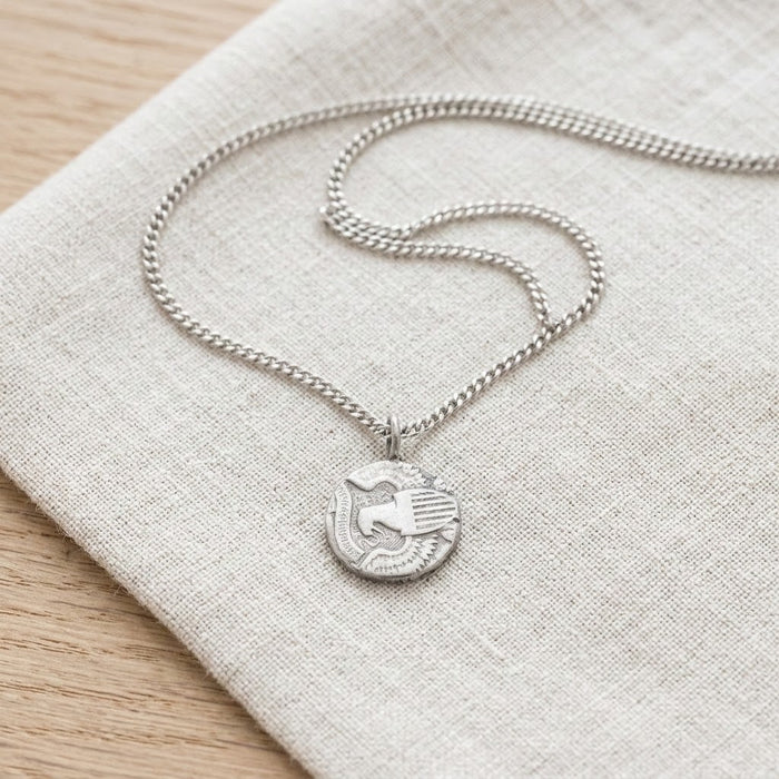 Round coin necklace resting on linen - Minted Jewellery