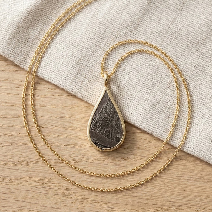 Seymchan meteorite teardrop necklace in yellow gold, on linen - Minted Jewellery